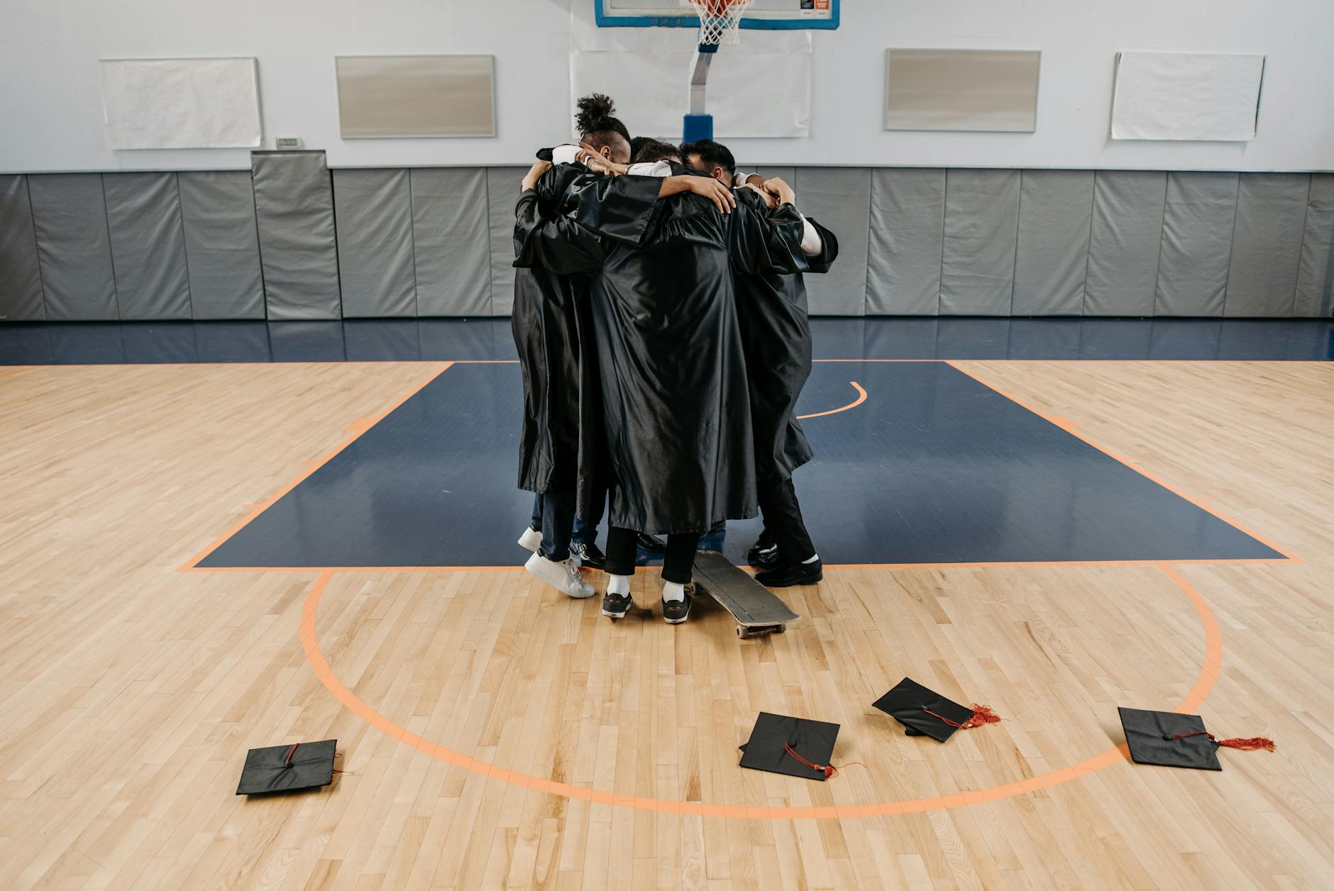 Absolwenci AWF w togach obejmują się radośnie na sali gimnastycznej